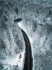 Aerial view of a red car traversing winding road in winter