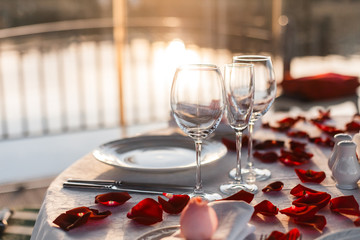 Romantic Valentine day dinner setting  with rose petals and empty wineglasses on sunset