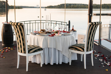 Romantic Valentine day dinner setting  with rose petals and empty wineglasses on sunset