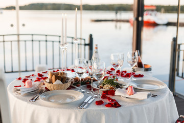 Romantic Valentine day dinner setting  with rose petals and empty wineglasses on sunset