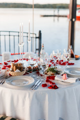 Romantic Valentine day dinner setting  with rose petals and empty wineglasses on sunset