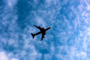 beautiful clear silhouette of the plane in the blue sky, against the background of white fluffy light cirrus clouds, travel by plane, long-distance flights, new technologies, high-speed transport