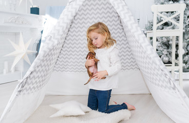 The little girl is playing with small puppy dog near the wigwam in christmas playroom © Irina84