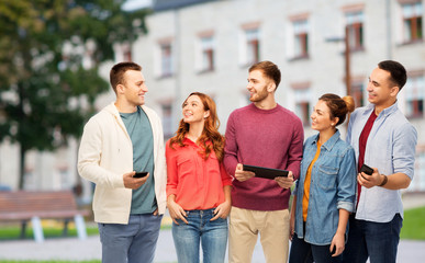 technology, education and people concept - group of smiling friends or students with smartphones and tablet computer over campus background