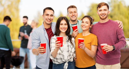 celebration, friendship and people concept - group of smiling friends toasting non alcoholic drinks in party cups over rooftop party background