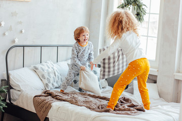 Brother and sister in pajamas playing with pillows on the bed