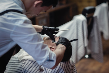 Hairdresser in black gloves shaves with a straight razor beard