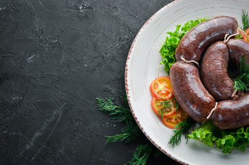 Bloody sausage in a plate with tomatoes and lettuce. Top view. Free space for your text.