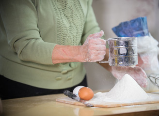 An old lady making little pies. Sifting the flour