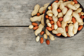 Roasted peanuts in the shell and peeled in a cup, against a gray wooden table