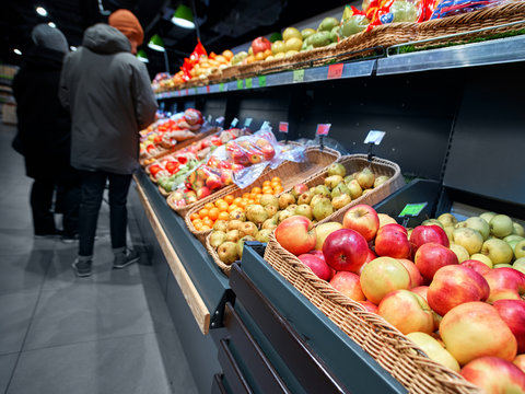 Fresh fruits and vegetables in grocery store. Couple of customers choosing fruit at the grocery department in the hypermarket. Showcase of many different apples and other fruits. Rich selection