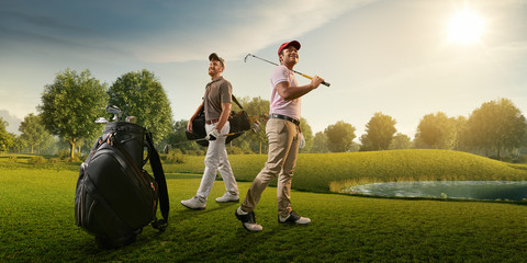 Two male golf players on professional golf course. Smiling golfers walking with golf clubs and golf...