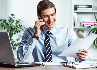 Manager man talking on the phone and looks at the documents. Photo of successful manager working with financial data in the office. Business concept