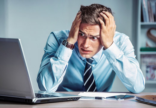 Shocked businessman dissatisfied his earnings, looking at laptop. Photo of young man working in the office. Business concept