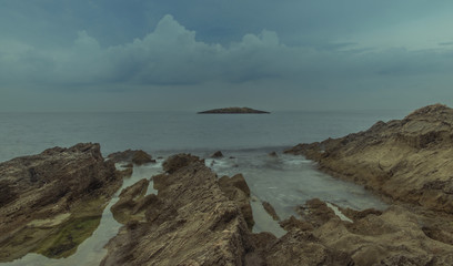 Fototapeta na wymiar Mallorca, Balearic Islands, Spain - October 12, 2018: Long exposure on a rocky beach at low tide, with a small island in the background