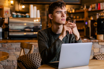 Thoughtful stylish guy with glasses sitting in a cozy cafe