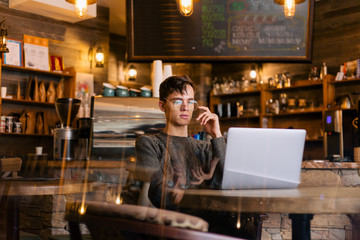 Stylish guy with glasses sitting in a cozy cafe working on a laptop developing a business plan