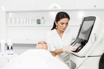 Beautician prepares equipment for facial rejuvenation procedures for the girl client lying on the couch