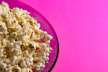 Full glass plate of fried popcorn on pink background with copy space. Concept of leisure