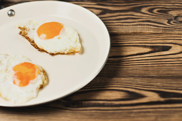 Two fried eggs in metal beige pan on old wooden brown table. Copy space
