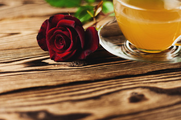 Glass cup with green tea and red rose on sprig on old wooden table. Saint Valentine's Day concept