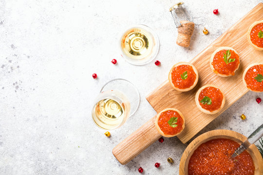 Christmas and New Year holidays composition. Red Salmon Caviar in wooden bowl, Tartlets Festive Appetizer and champagne on  gray background.Copy space for Text.