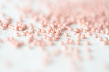 Pink seed beads scattered on textile background close up	