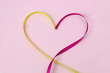 A heart of yellow and pink satin ribbons on a pink background by 14 February , Valentine's Day as a...