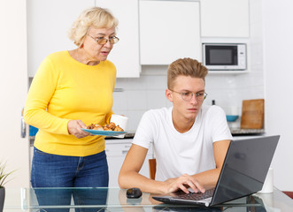 Guy sitting while mom serving him cookies