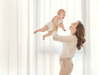 Mother with a baby in her arms plays against the window. 