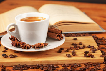 Coffee break with a Cup of hot strong coffee on a wooden table with an open old book covered with cloth. A white Cup of black coffee surrounded by a small amount of roasted coffee beans
