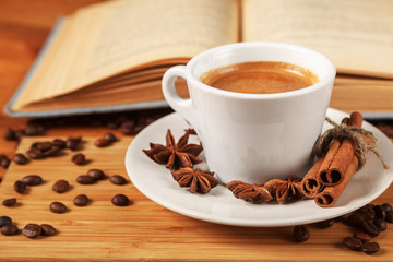 Coffee break with a Cup of hot strong coffee on a wooden table with an open old book covered with cloth. A white Cup of black coffee surrounded by a small amount of roasted coffee beans