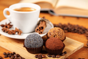 Coffee break a Cup of hot coffee and cakes on a wooden table with an open book. A white Cup of black coffee surrounded by a small amount of roasted coffee beans, cinnamon and cinnamon