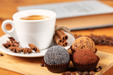 Coffee break a Cup of hot coffee and cakes on a wooden table with a book. A white Cup of black coffee surrounded by a small amount of roasted coffee beans, cinnamon and anise