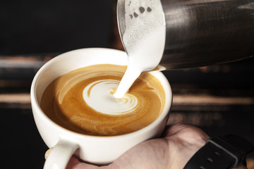 A professional Barista holds a Cup of coffee, making a beautiful heart shape latte art. Hot art latte coffee with heart shape in white Cup