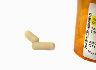 close up of two drug capsules with orange prescription bottle isolated on white