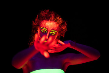 A beautiful young sexy girl with ultraviolet paint on her body dancing in the dark. Pretty woman with glowing bodyart in black lamp light