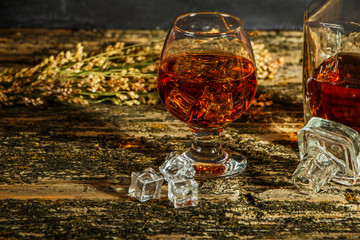 Whiskey with ice in a glass on an old dark tree table. Whiskey or cognac on a wooden dark table....