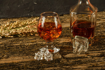 Whiskey with ice in a glass on an old dark tree table. Whiskey or cognac on a wooden dark table. Whiskey. Selective focus.