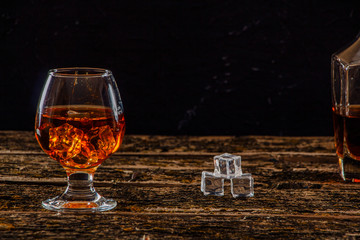 Whiskey with ice in a glass on an old dark tree table. Whiskey or cognac on a wooden dark table. Whiskey. Selective focus.