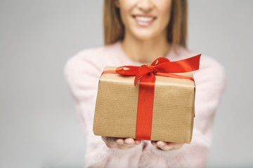 Image of Happy brunette woman in casual holding gift box and looking at the camera isolated over white background. Close-up.