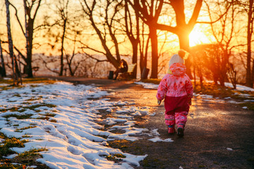 young little toddler girl walking by city park on sunset. view from behind