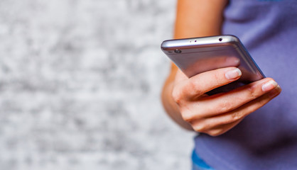 young teenager girl hand using mobile phone or smartphone on gray wall background