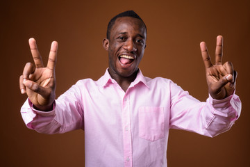 Portrait of young African businessman making peace sign against brown background
