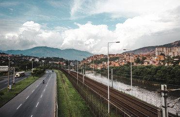 Fototapeta premium Highway, river and railway in the lush valley city of Medellín, Colombia, with the red houses of barrios built into the hills