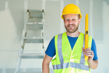 Caucasian Male Contractor With Hard Hat, Level and Safety Vest At Construction Site