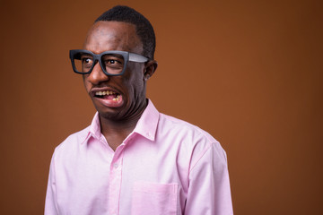 Portrait of young African businessman making faces against brown background