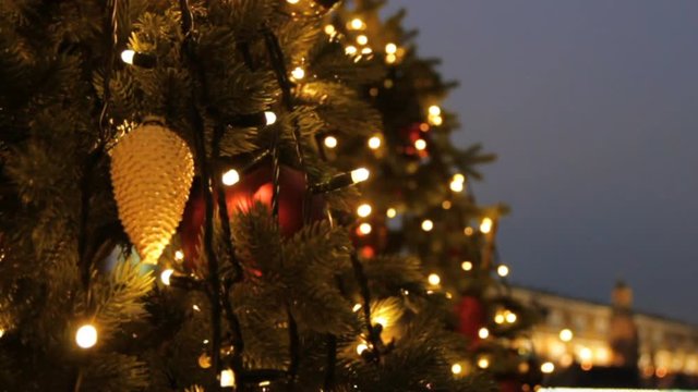 Holidays in Moscow. In the square a Christmas tree glows, decorated with balls and beautiful Christmas garland lights close-up. Kremlin tower, pedestrians and travellers walk on blurred background