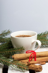 Obraz na płótnie Canvas A cup of coffee and Cinnamon sticks next to the fir branches. On a wooden box.