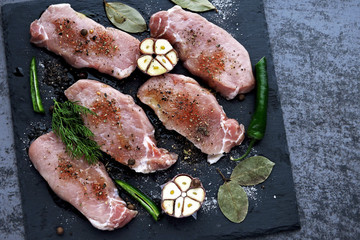 Raw pork steaks with spices on a stone board for a presentation. Pork steaks are marinated in...